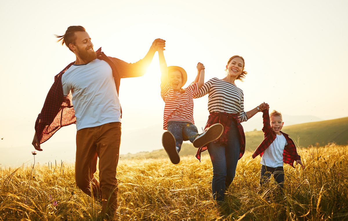 A family running together through a field at sunset